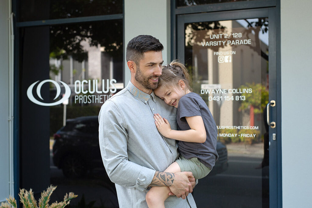 dwayne-collins-and-daughter Ocularist Dwayne Collins standing outside Oculus Prosthetics clinic on Queensland Gold Coast - Australia.